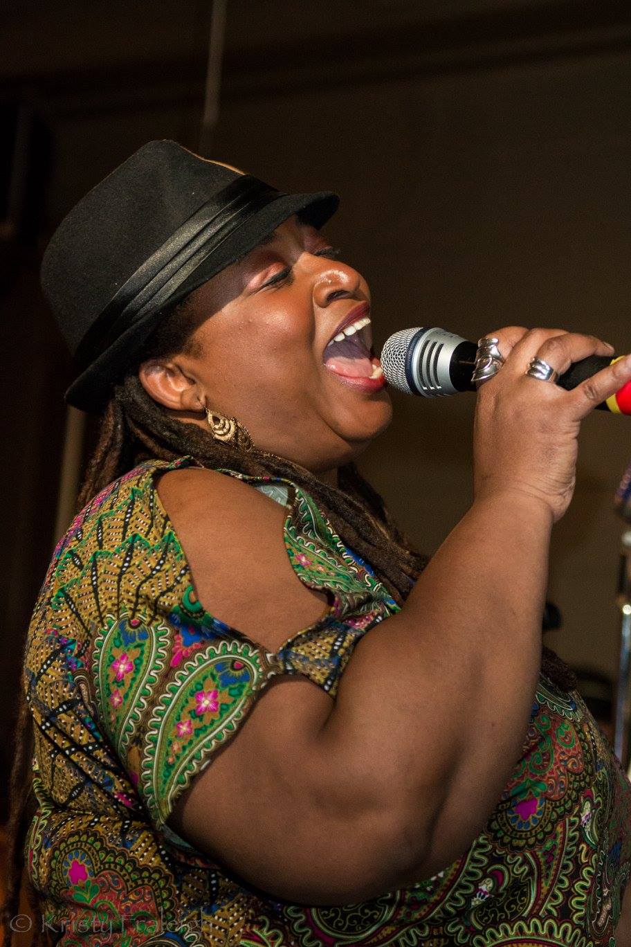 Carolyn T mid-song in a fedora